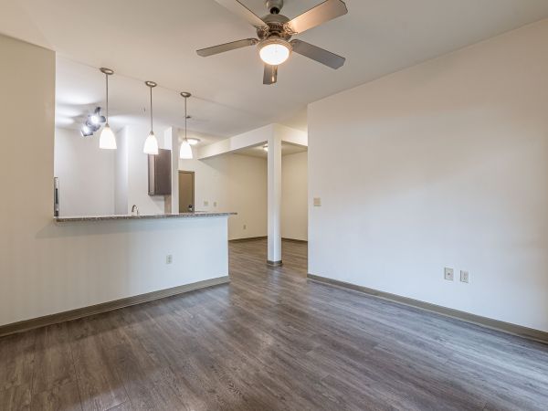 Empty modern room with wood floors, ceiling fan, and kitchen area with hanging pendant lights at Apex West Midtown.