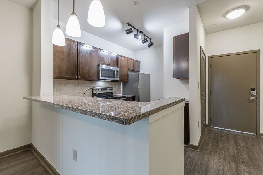Modern kitchen with granite countertops, stainless steel appliances, and pendant lighting near an entrance door at Apex West Midtown.
