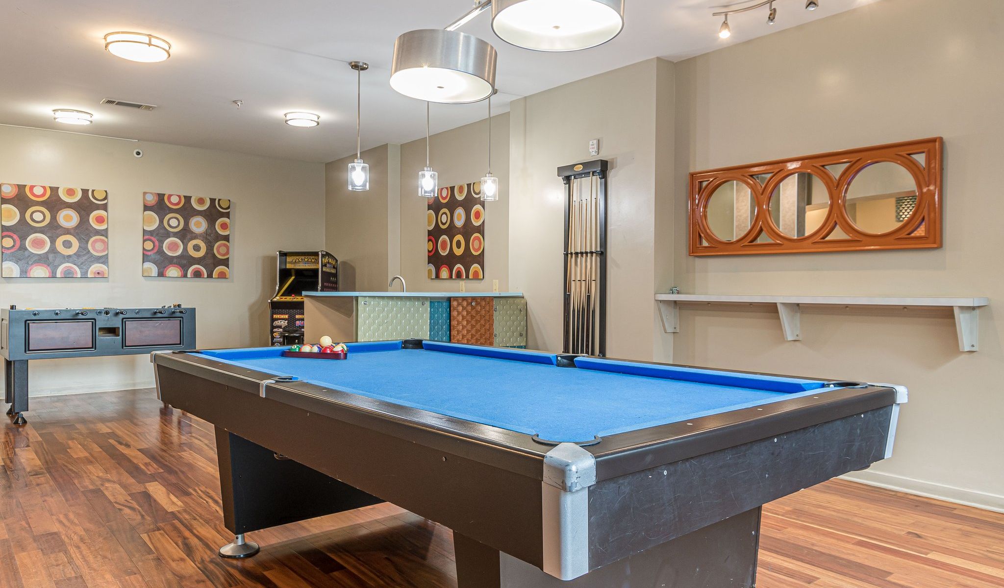 A modern game room with a blue pool table, foosball table, and colorful wall art on wood flooring Apex West Midtown