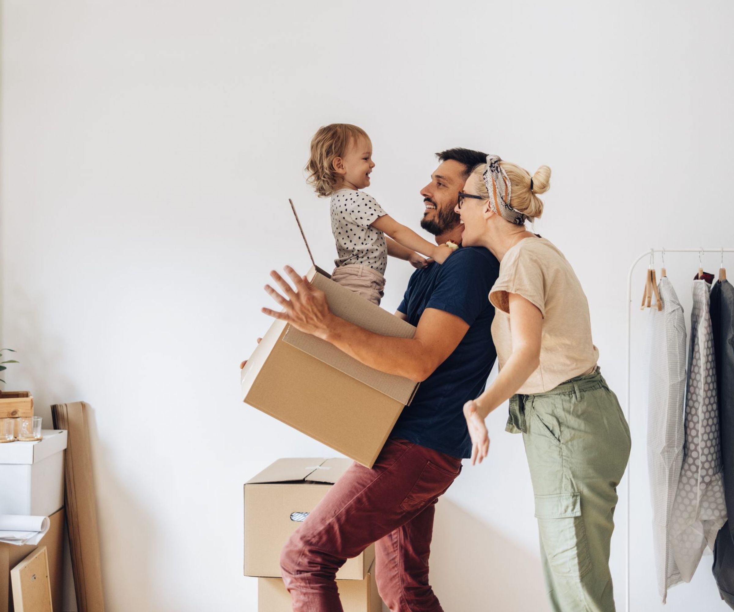 A smiling family carries moving boxes in a new home, with a child laughing in a parent's arms.