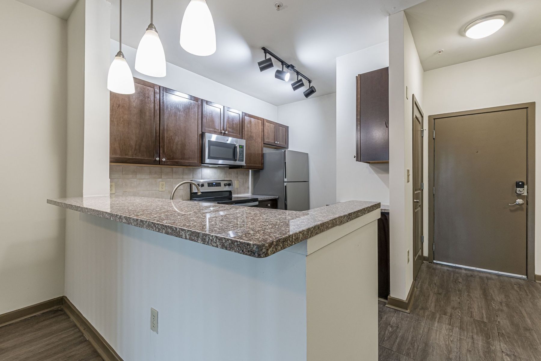 Modern kitchen with granite countertops, stainless steel appliances, and pendant lighting near an entrance door at Apex West Midtown.