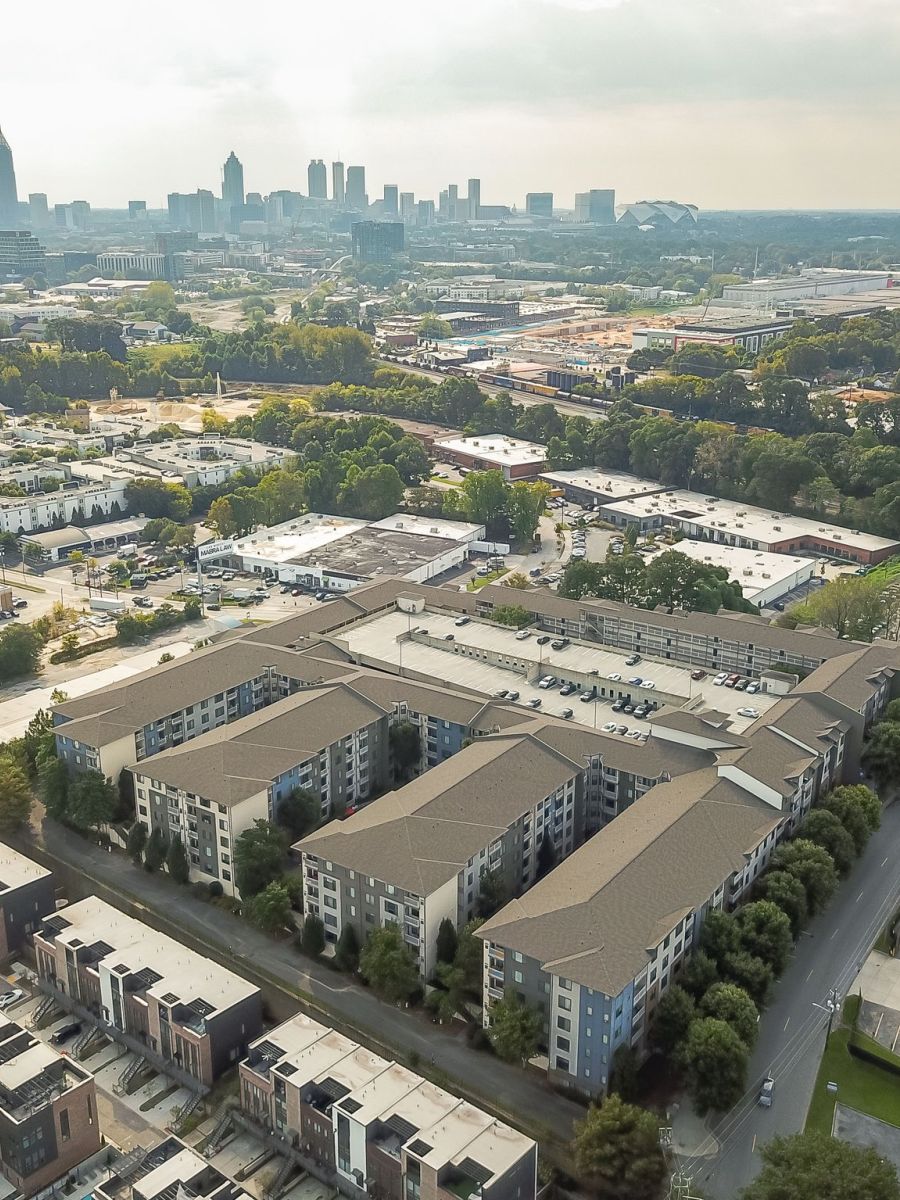 Aerial view of Apex West Midtown apartment buildings with a city skyline in the background on a cloudy day.