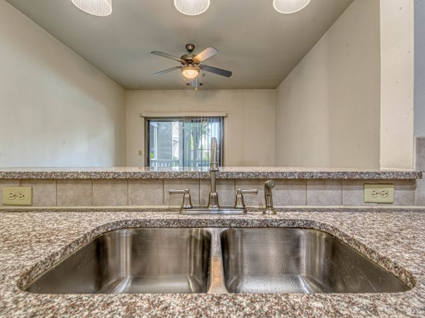 Double kitchen sink with granite countertop, backsplash, and view of ceiling fan and sliding glass door at Apex West Midtown.