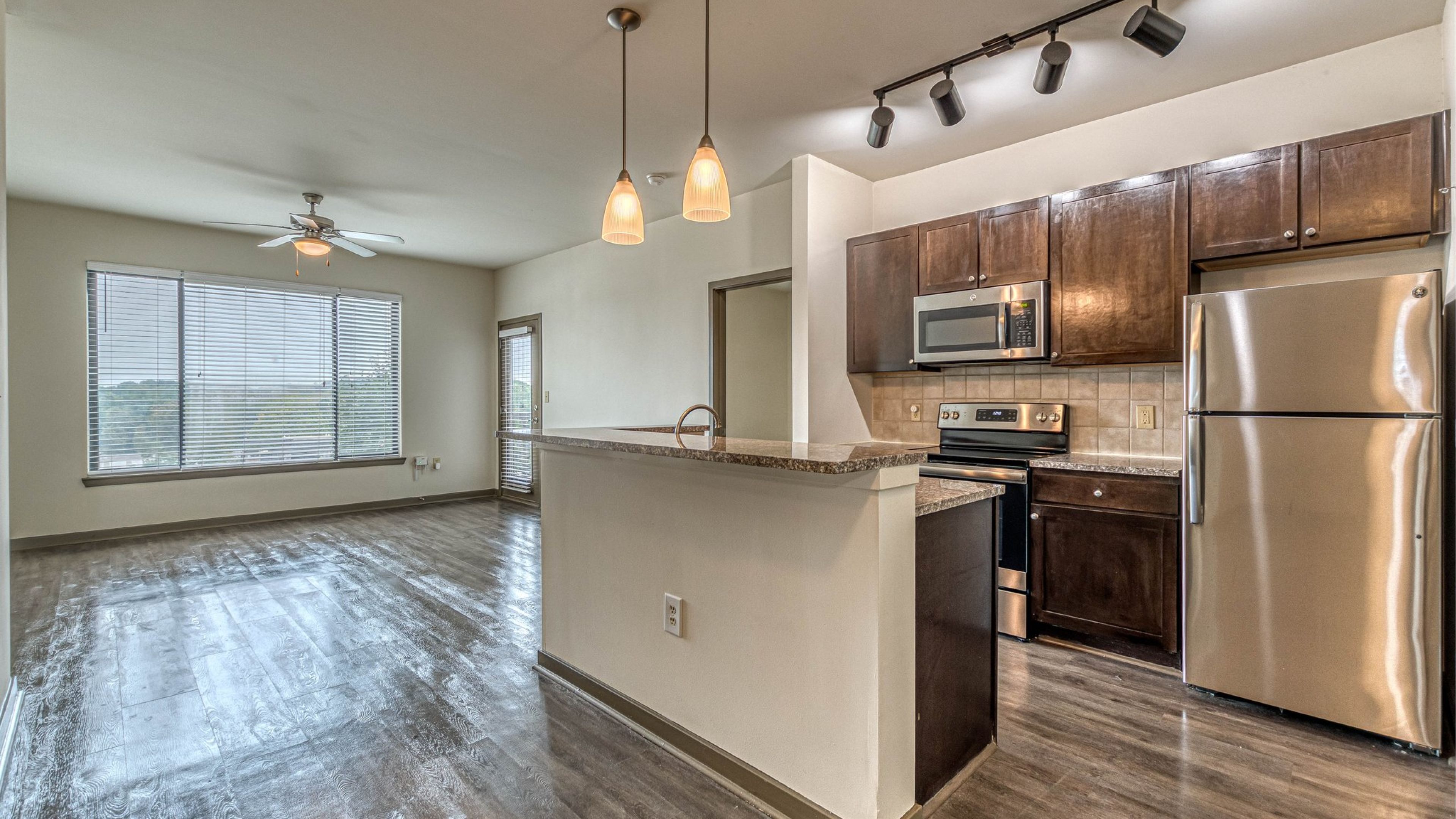 Modern apartment kitchen with stainless steel appliances, island, and open living area with large windows at Apex West Midtown.