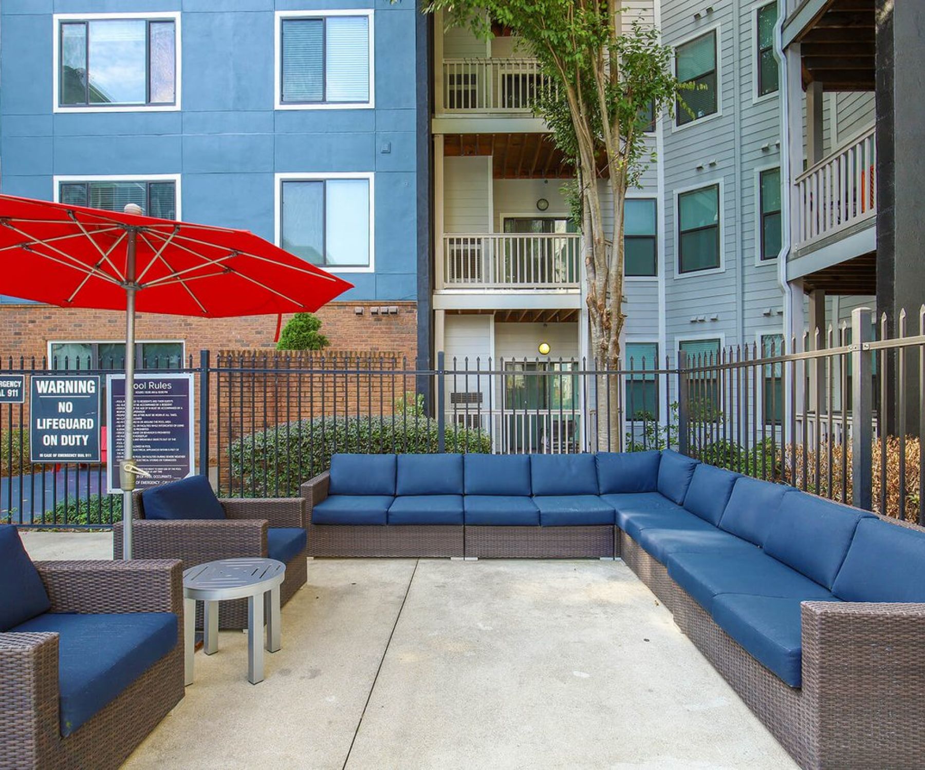 Apex West Midtown outdoor patio area with blue cushioned seating, a red umbrella, and apartment buildings in the background.