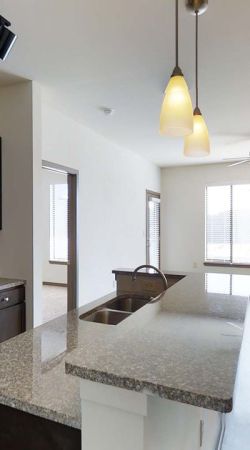Modern kitchen with dark cabinets, stainless steel appliances, and an island, opening to a bright living area.