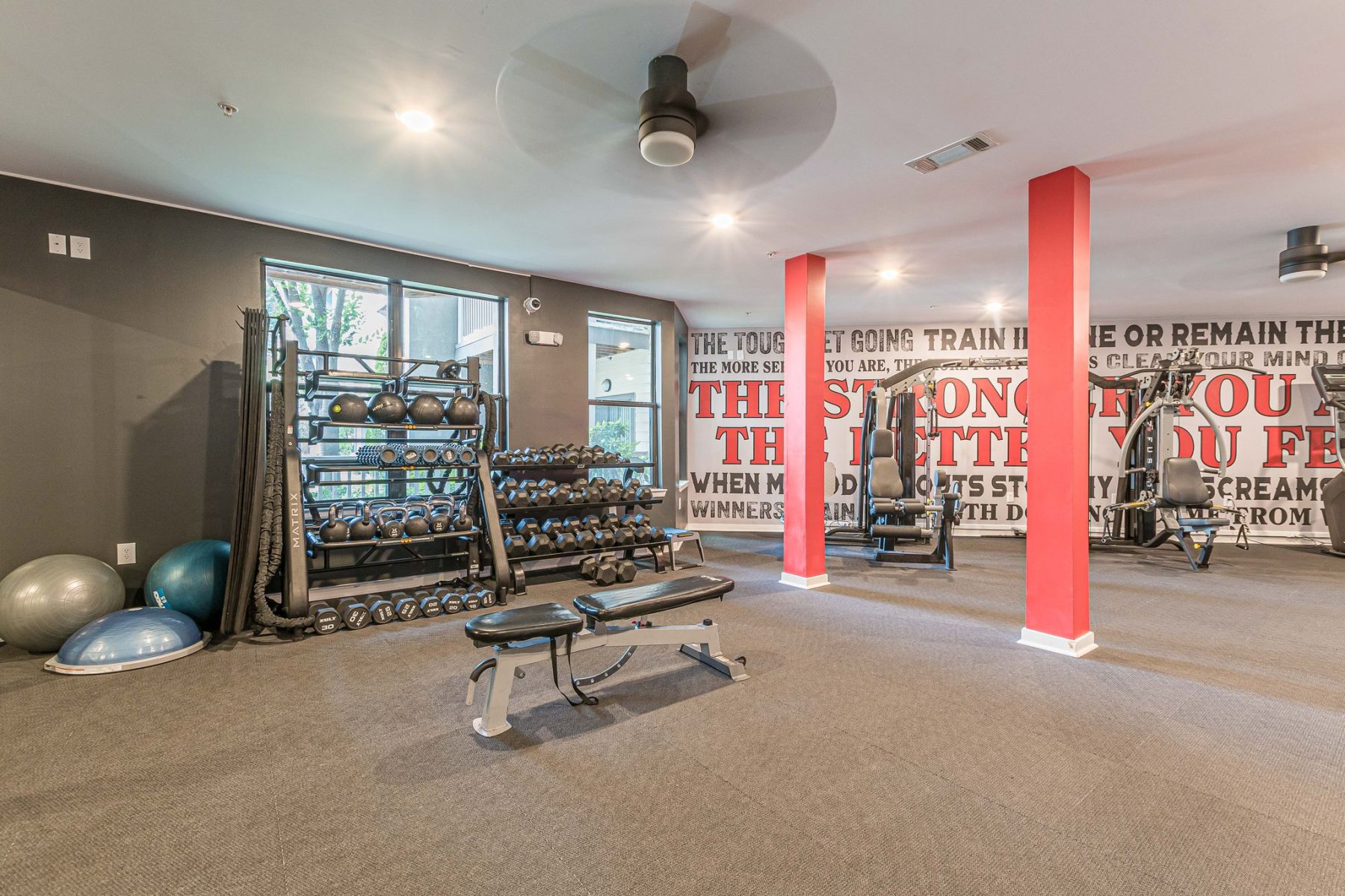 Apex West Midtown gym with dumbbells, kettlebells, benches, red pillars, and motivational wall text.