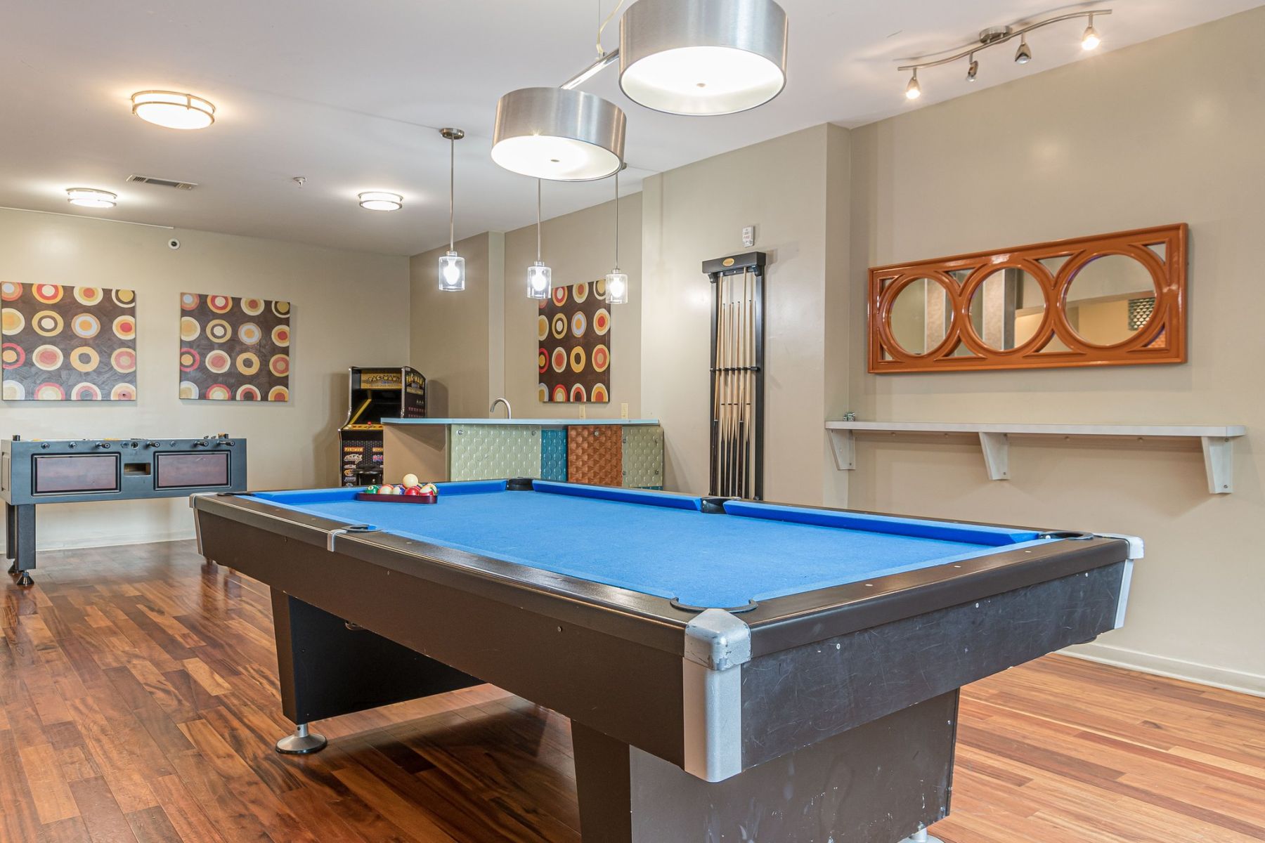 A modern game room with a blue pool table, foosball table, and colorful wall art on wood flooring Apex West Midtown
