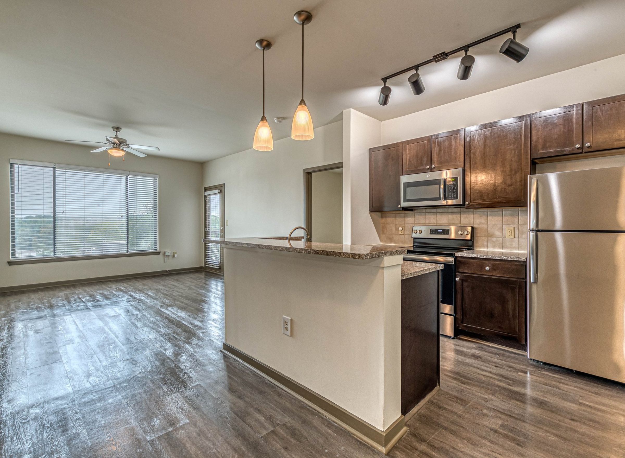 Modern apartment kitchen with stainless steel appliances, island, and open living area with large windows at Apex West Midtown.