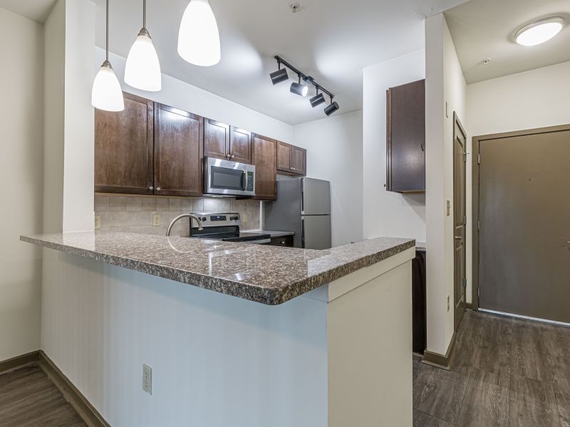 Modern kitchen with granite countertops, stainless steel appliances, and pendant lighting near an entrance door at Apex West Midtown.