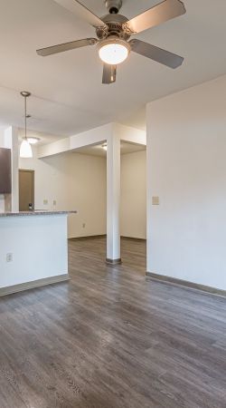 Empty modern room with wood floors, ceiling fan, and kitchen area with hanging pendant lights at Apex West Midtown.