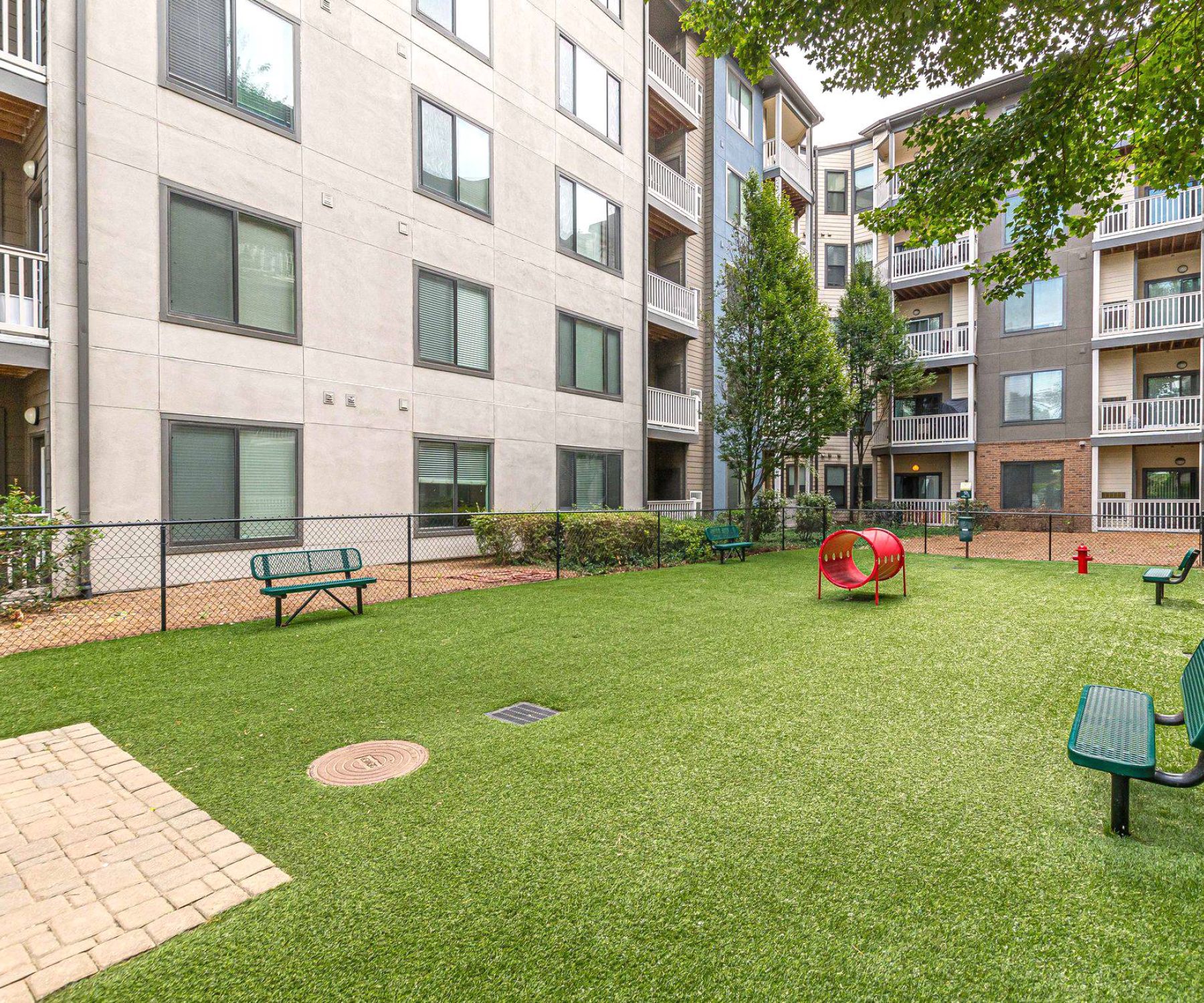Apex West Midtown 
 fenced grassy courtyard with benches and a red tunnel, surrounded by apartment buildings.