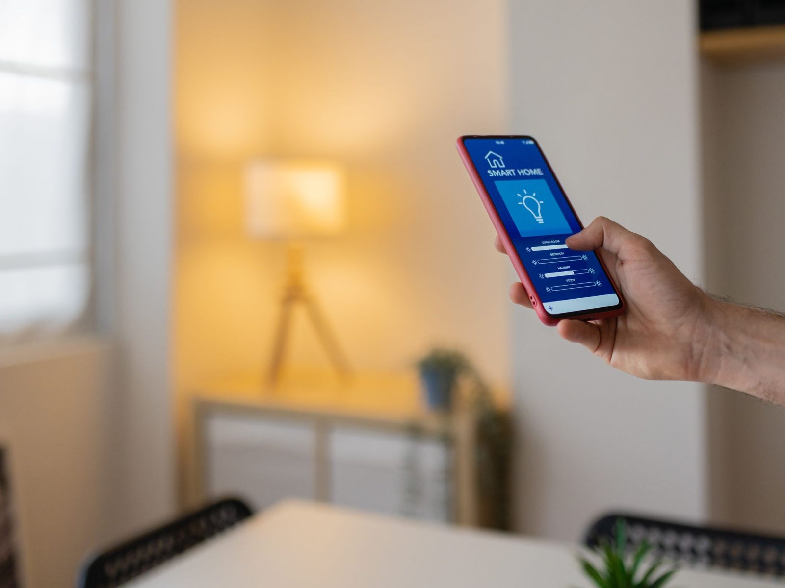 A person uses a smartphone app to control smart home lighting in a modern, softly lit room.