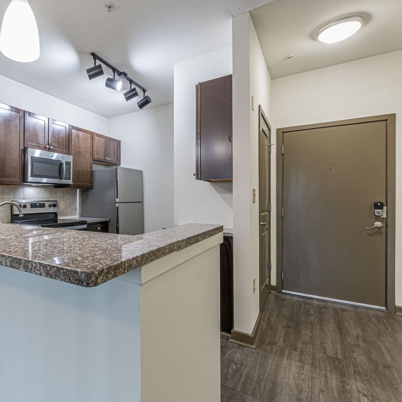 Modern kitchen with granite countertops, stainless steel appliances, and pendant lighting near an entrance door at Apex West Midtown.