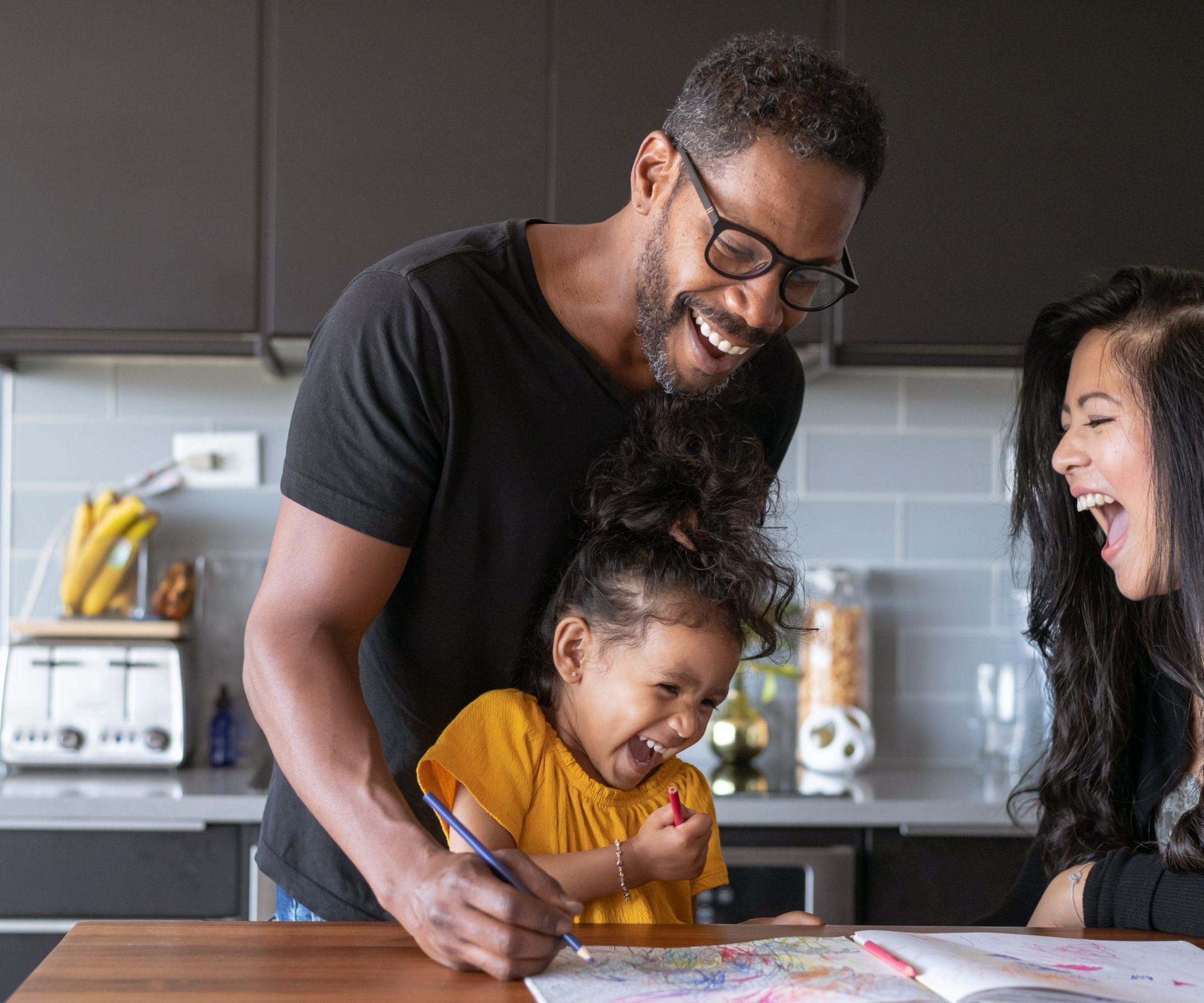 Smiling family drawing together at a kitchen table, laughing and enjoying each other's company.