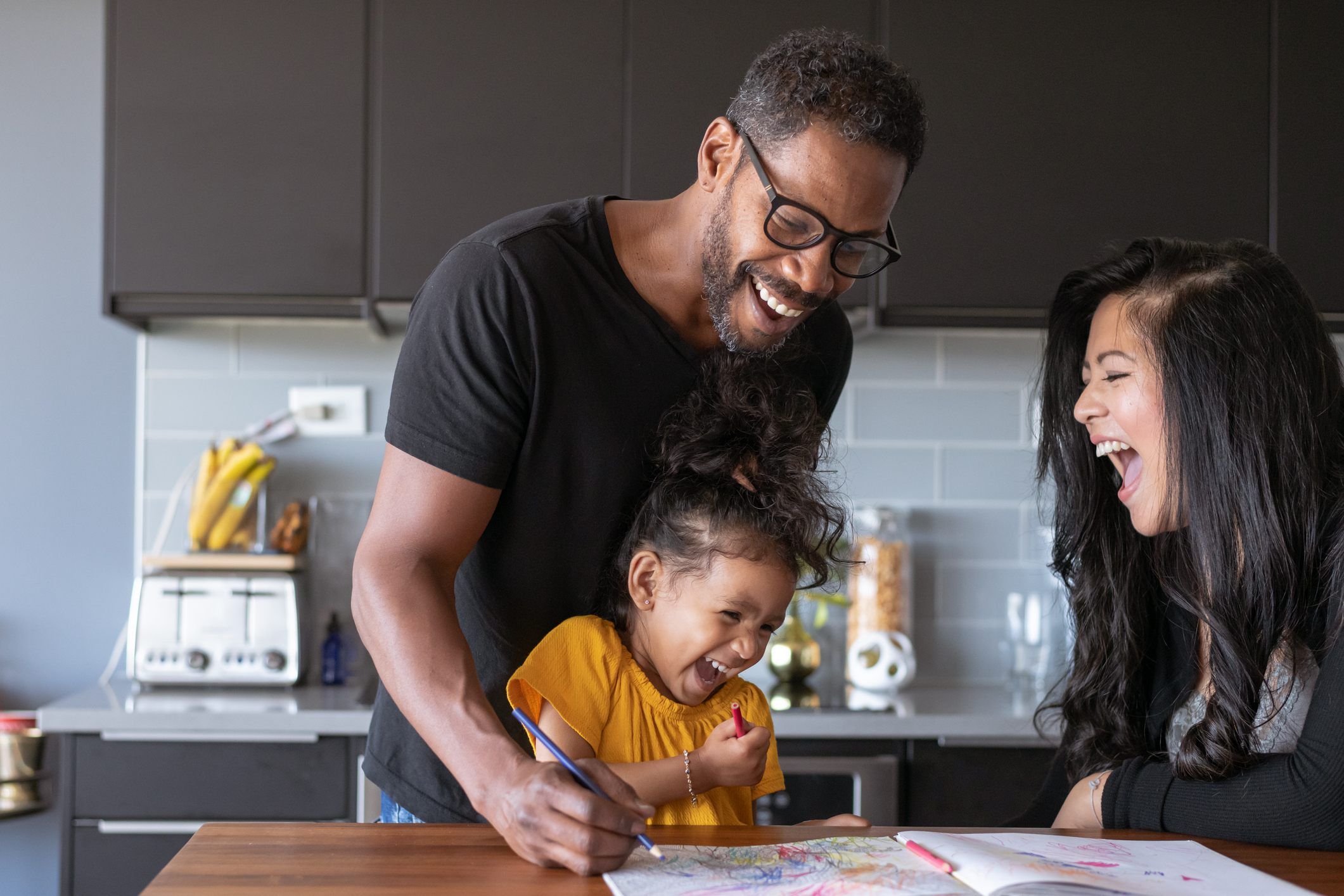Smiling family drawing together at a kitchen table, laughing and enjoying each other's company.