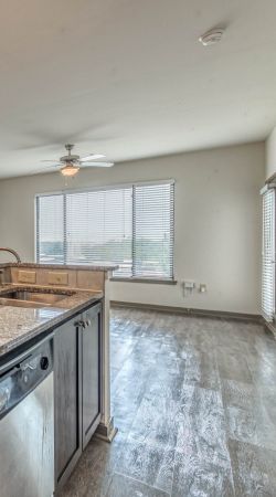 Modern kitchen with granite countertops, pendant lights, and an open living area with large windows Apex West Midtown.