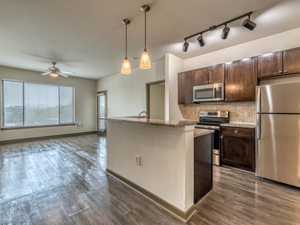 Modern apartment kitchen with stainless steel appliances, island, and open living area with large windows at Apex West Midtown.