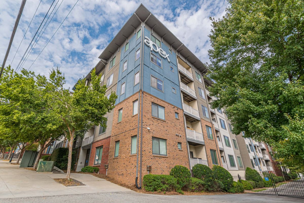 Apex West Midtown mid-rise apartment building with "apex" sign, surrounded by trees and a gated entrance.