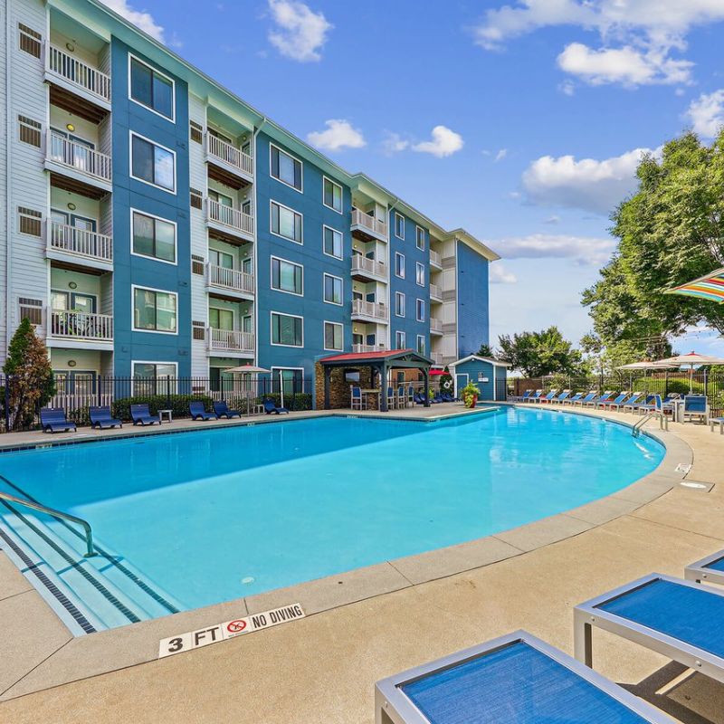 Apex West Midtown pool with blue lounge chairs, umbrellas, and four-story buildings in the background.