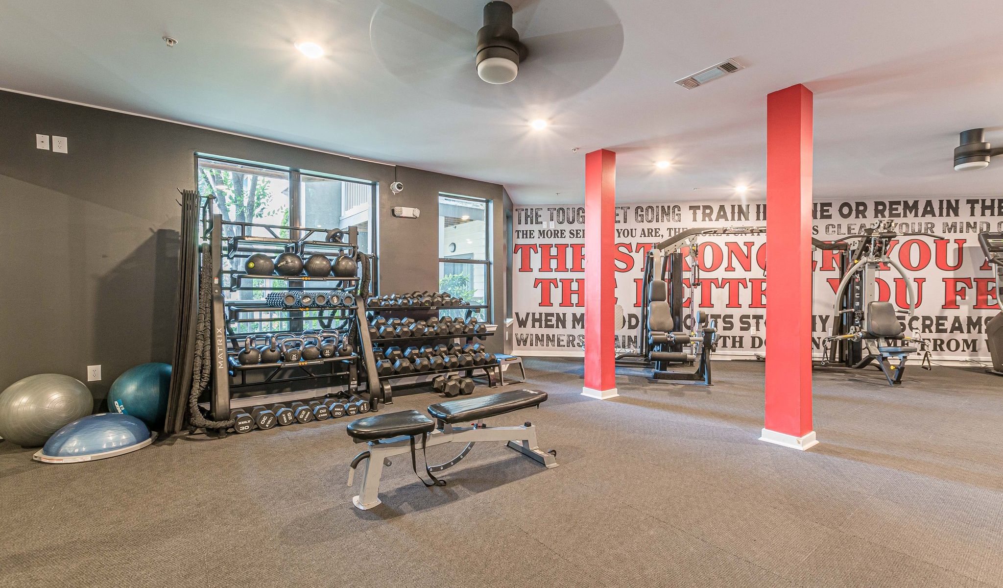 Modern gym room with free weights, kettlebells, benches, and motivational quotes on the wall at Apex West Midtown