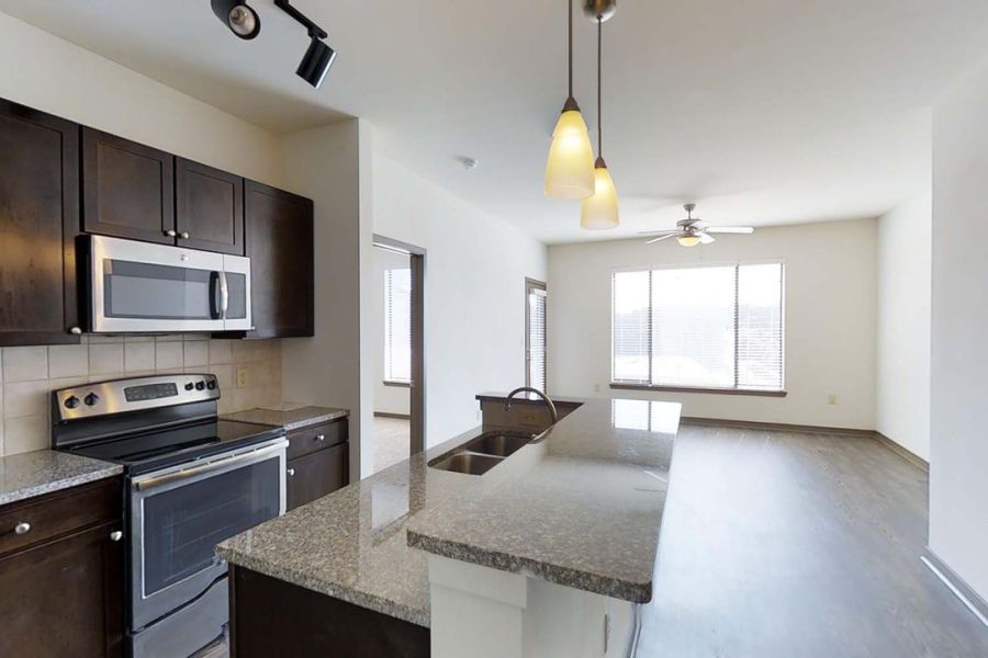 Modern kitchen with dark cabinets, stainless steel appliances, and an island, opening to a bright living area.