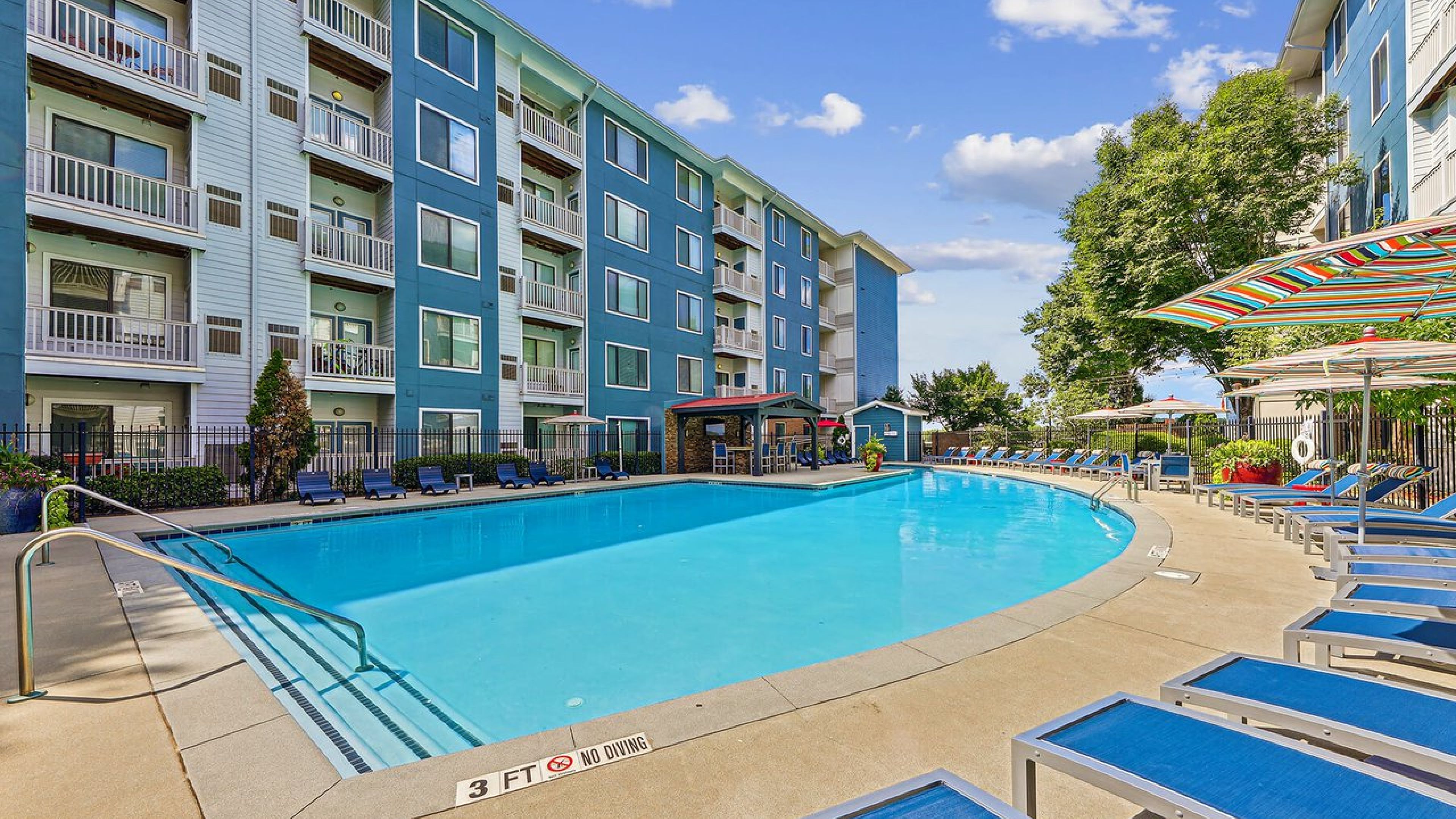 Apex West Midtown pool with blue lounge chairs, umbrellas, and four-story buildings in the background.